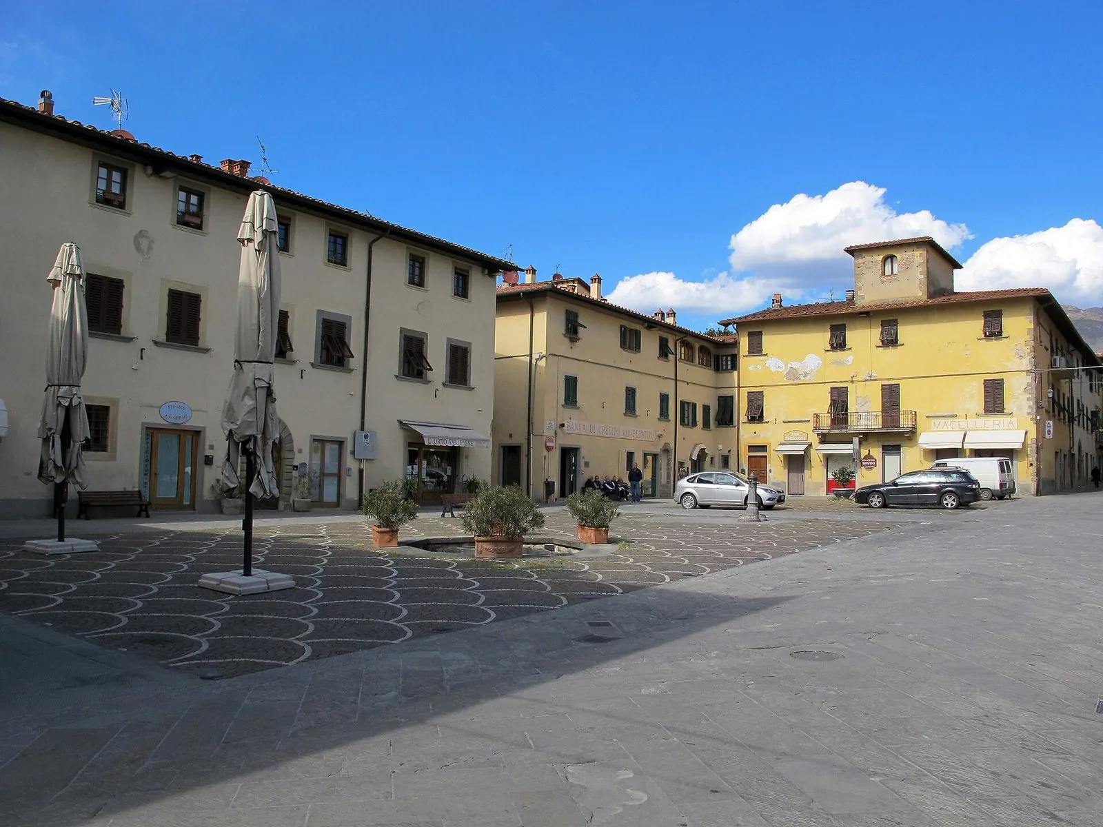 Piazza Vittorio Emanuele a Castelfranco di Sopra con palazzi color crema e ocra, cielo azzurro e nuvole bianche