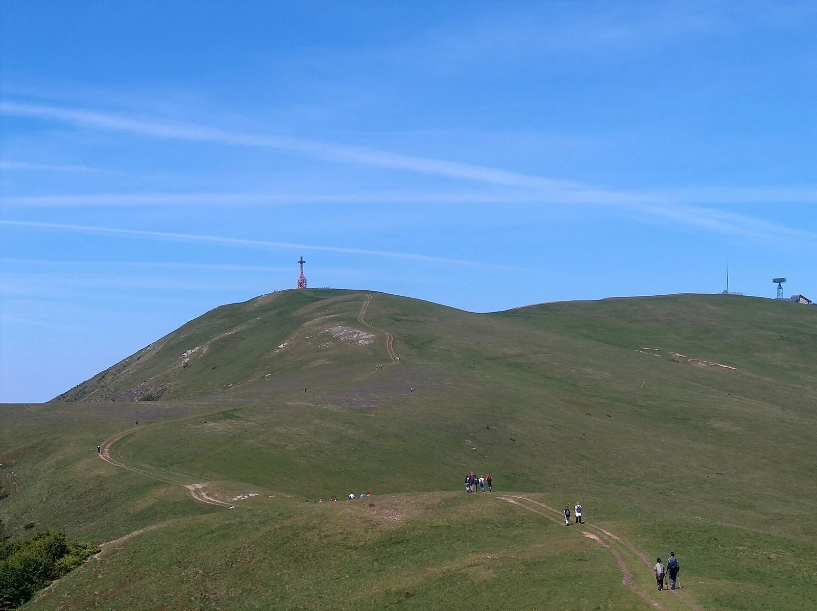 Il crinale erboso del Pratomagno con la croce in cima e un sentiero percorso da escursionisti lontani